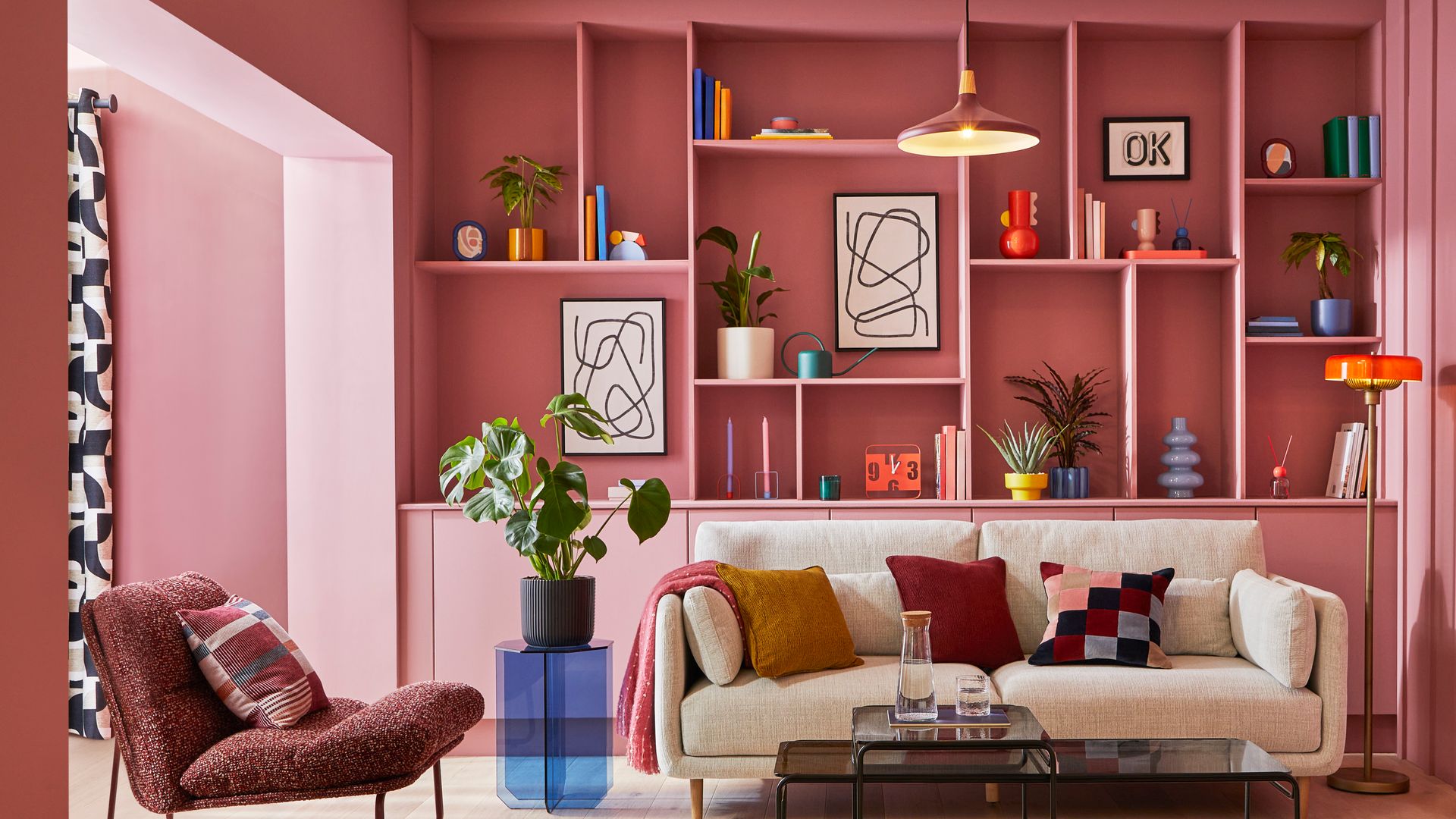 Salón con librería y paredes en color rosa claro, sofá beige, alfombra de colores, mesa auxiliar azul, mesa de centro negra