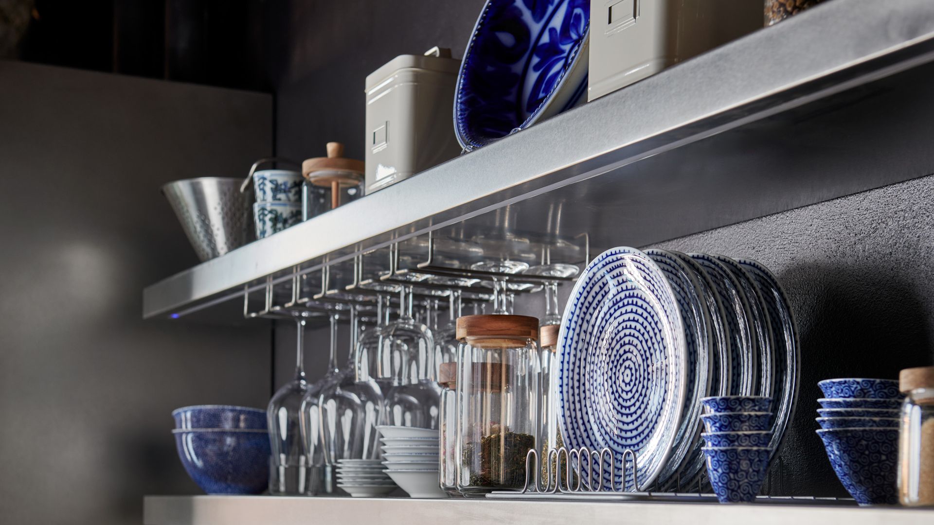 Baldas de cocina con copas colgando, platos azules, cuencos azules de porcelana, botes de cristal 
