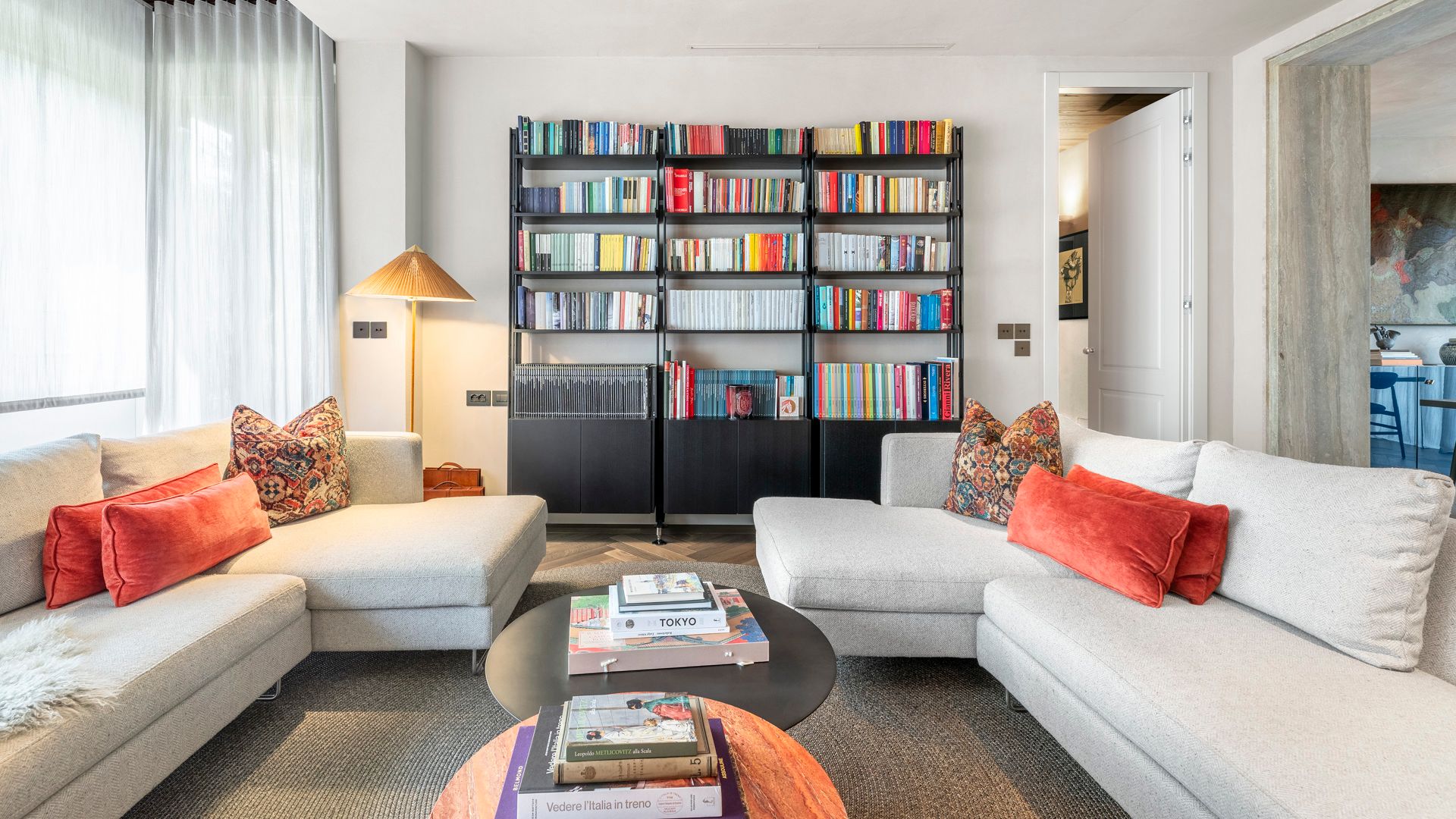 Salón con gran librería negra llena de libros, sofás blancos, mesa de centro negra y cortinas blancas