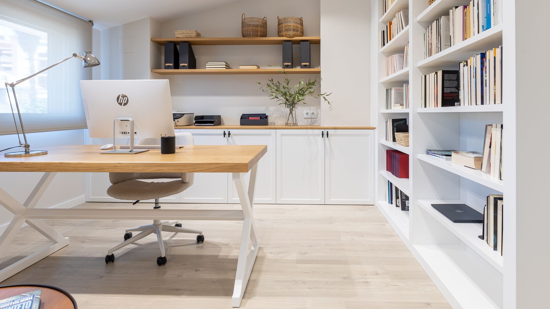 Despacho en casa con mueble a medida que recorre la pared, estanterías, baldas, mesa de escritorio con el sobre de madera, ordenador 