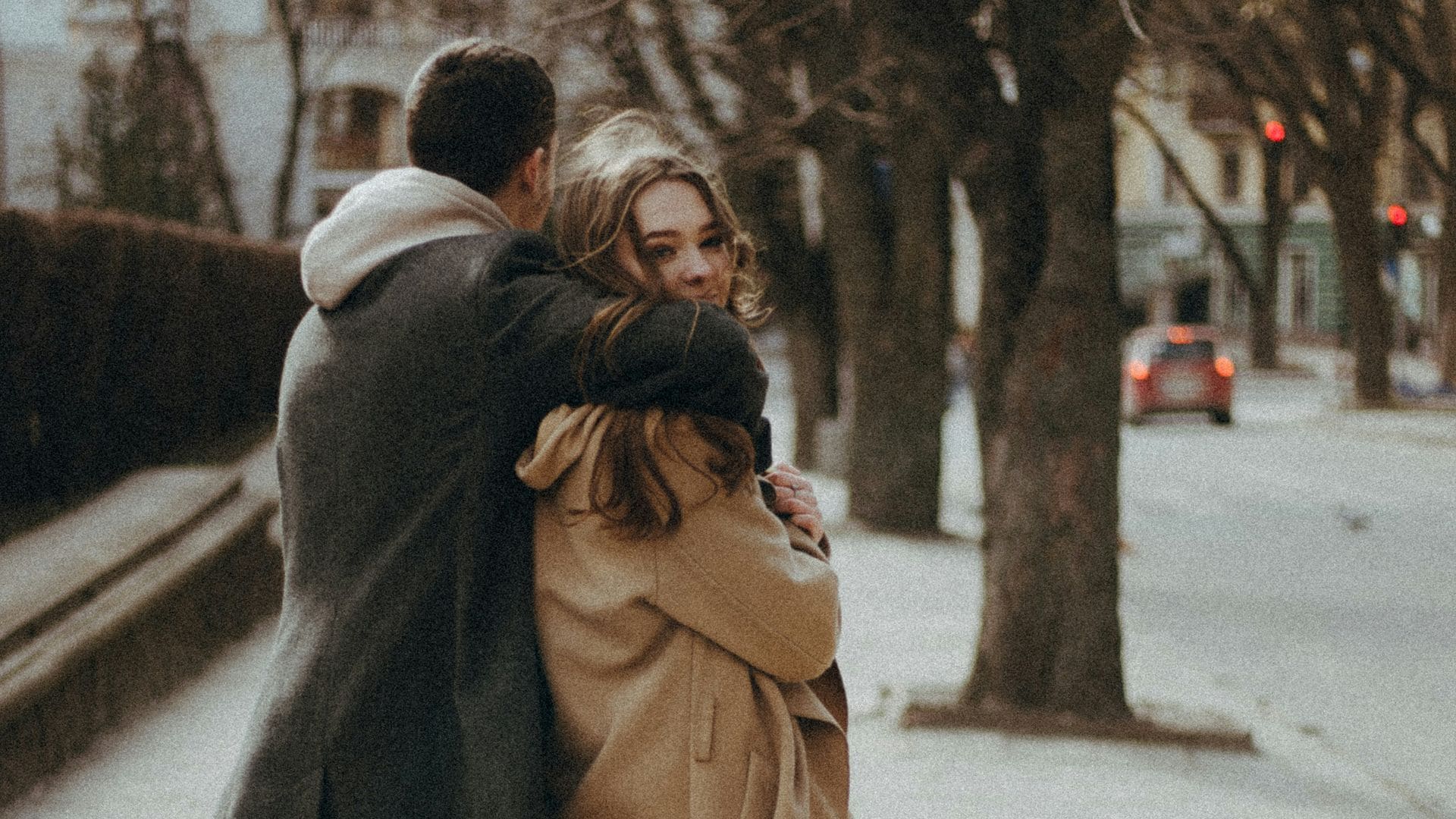Pareja paseando sonriente por la ciudad, abrazados. Van de espaldas, pero ella mira a la cámara.
