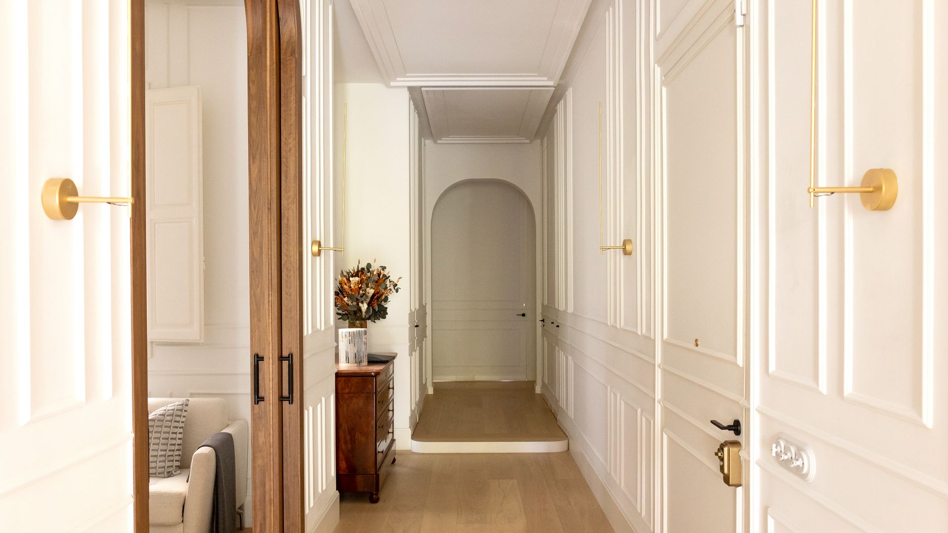 Entrada casa, pasillo con molduras en las paredes y en las puertas, suelo de madera, sofá blanco, puerta corredera de madera 