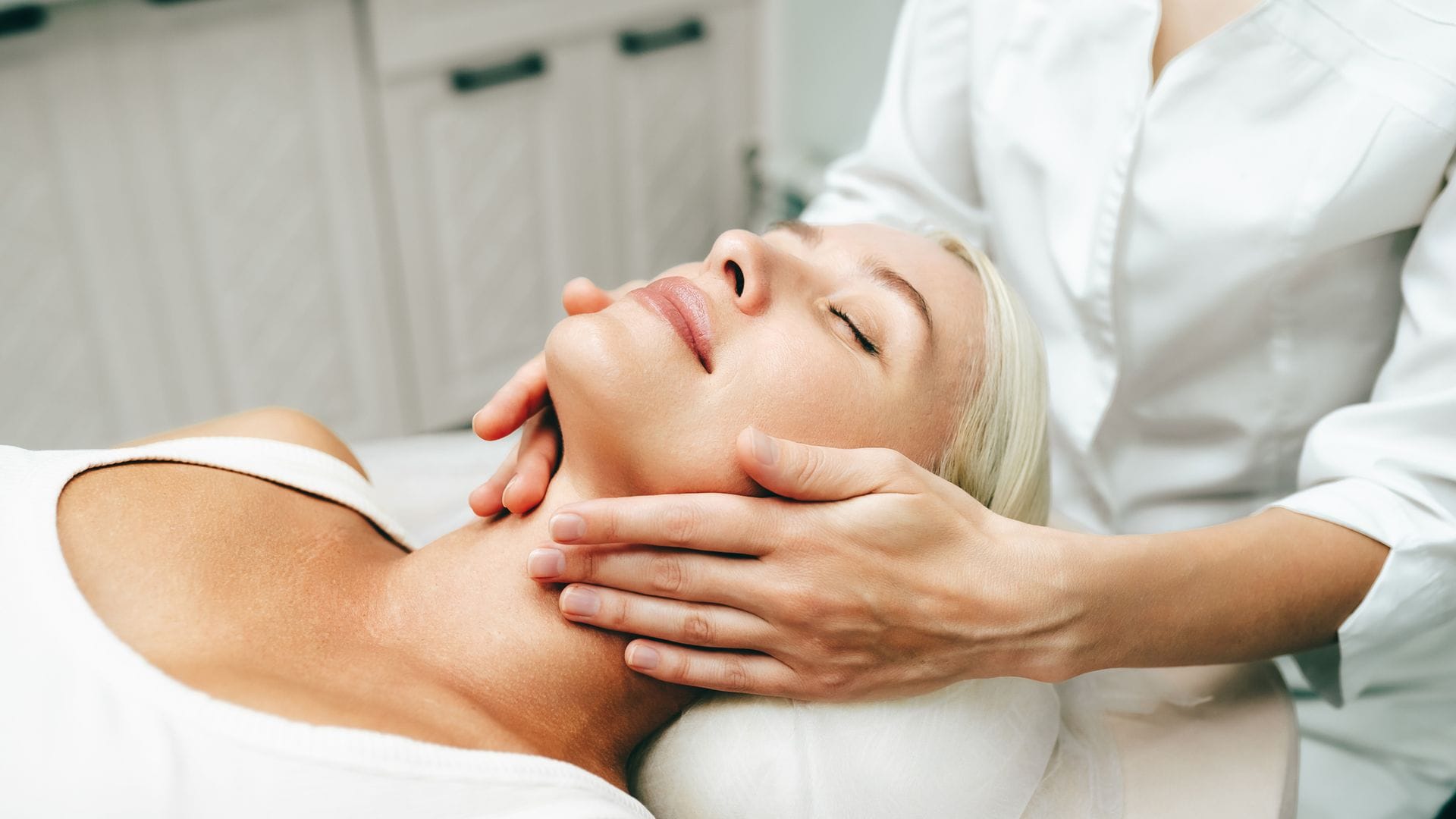 Mujer adulta tumbada en camilla con ojos cerrados mientras le aplican tratamiento en el cuello