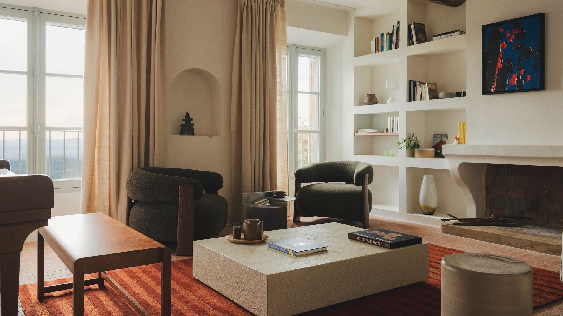 Salón con chimenea y librería de obra, con alfombra de rayas, cortinas, vigas de madera en el techo, mesa de centro de piedra natural, butacas 