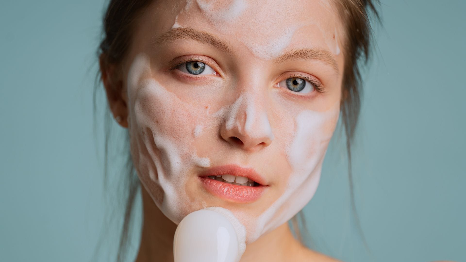 Rostro de mujer joven con pelo castaño claro limpiando su cara con jabón