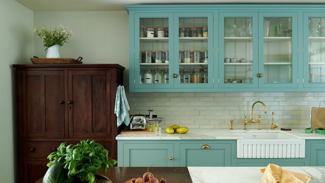 Cocina con muebles azules, vitrinas superiores, alacena de madera, mesa de madera, fregadero antiguo y grifo dorado