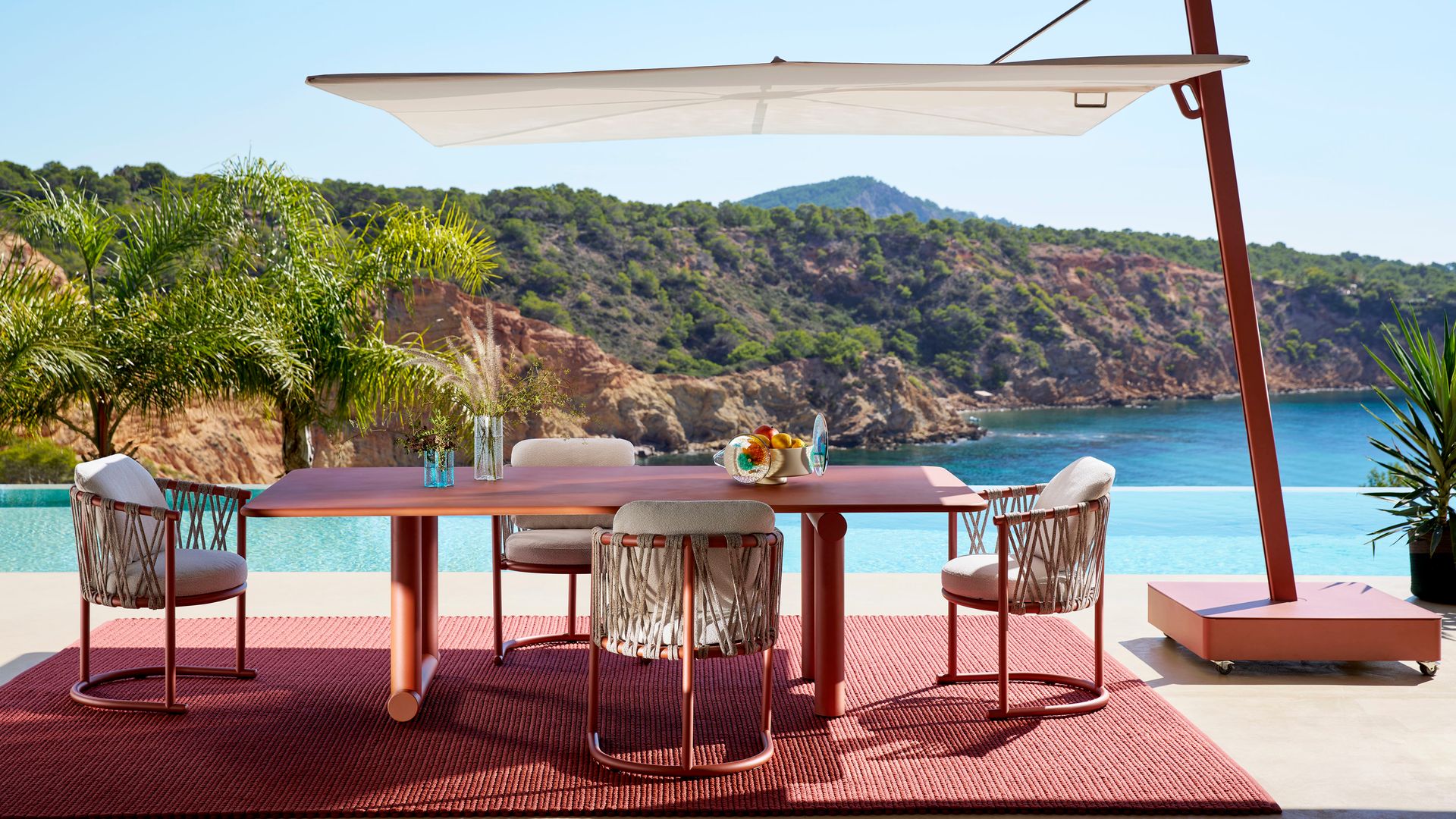 Muebles de exterior de color rojo, con alfombra de fibras vegetales roja, sombrilla tipo vela con el pie rojo