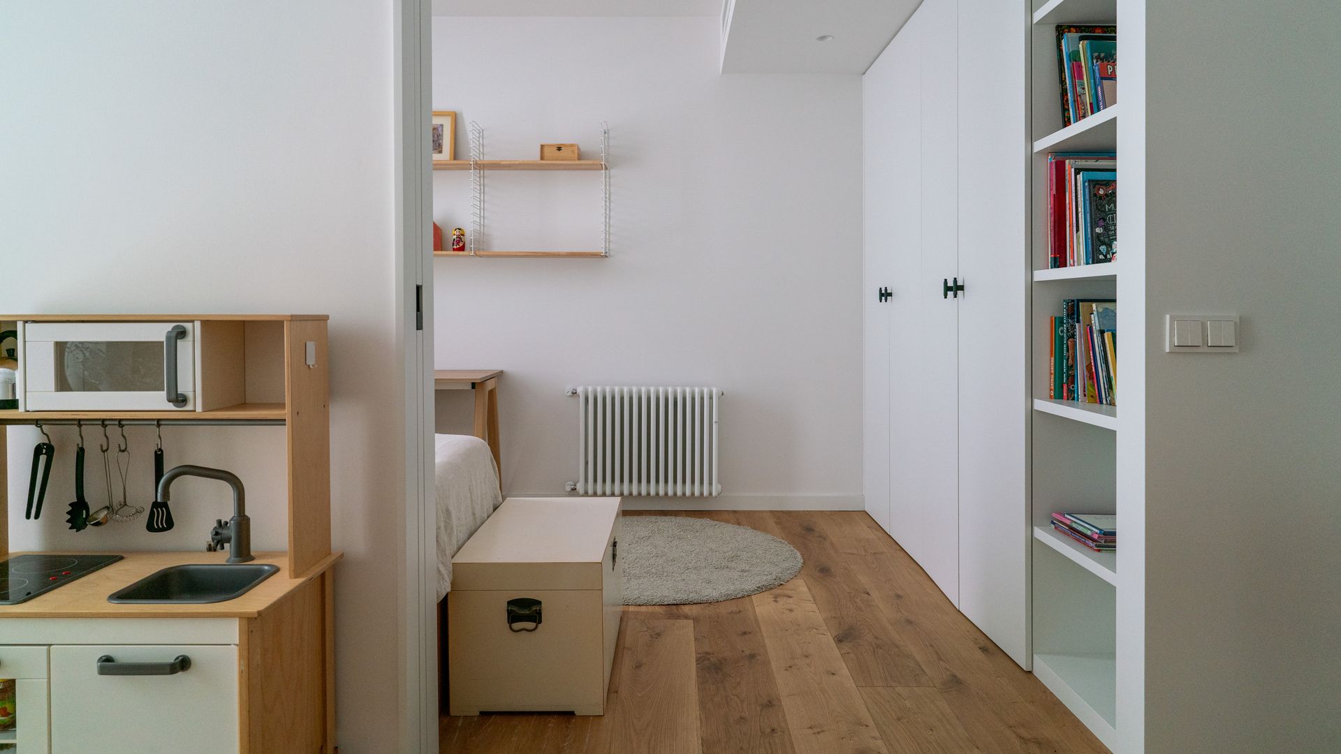 Dormitorio con armario blanco a medida, radiador blanco y cocinita infantil 
