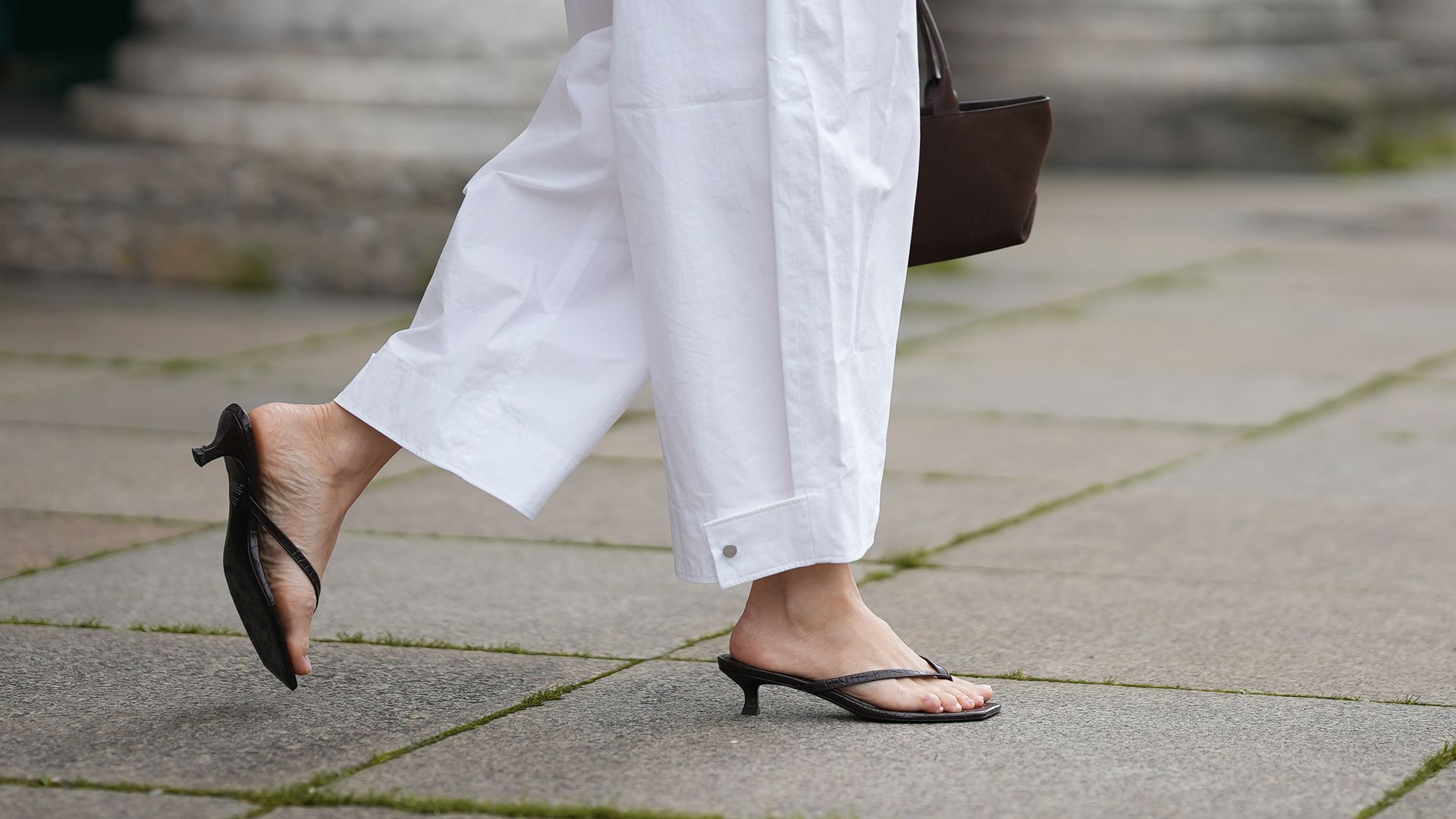 Piernas de mujer caminando por la calle con pantalones blancos anchos y sandalias de dedo con tacón mini