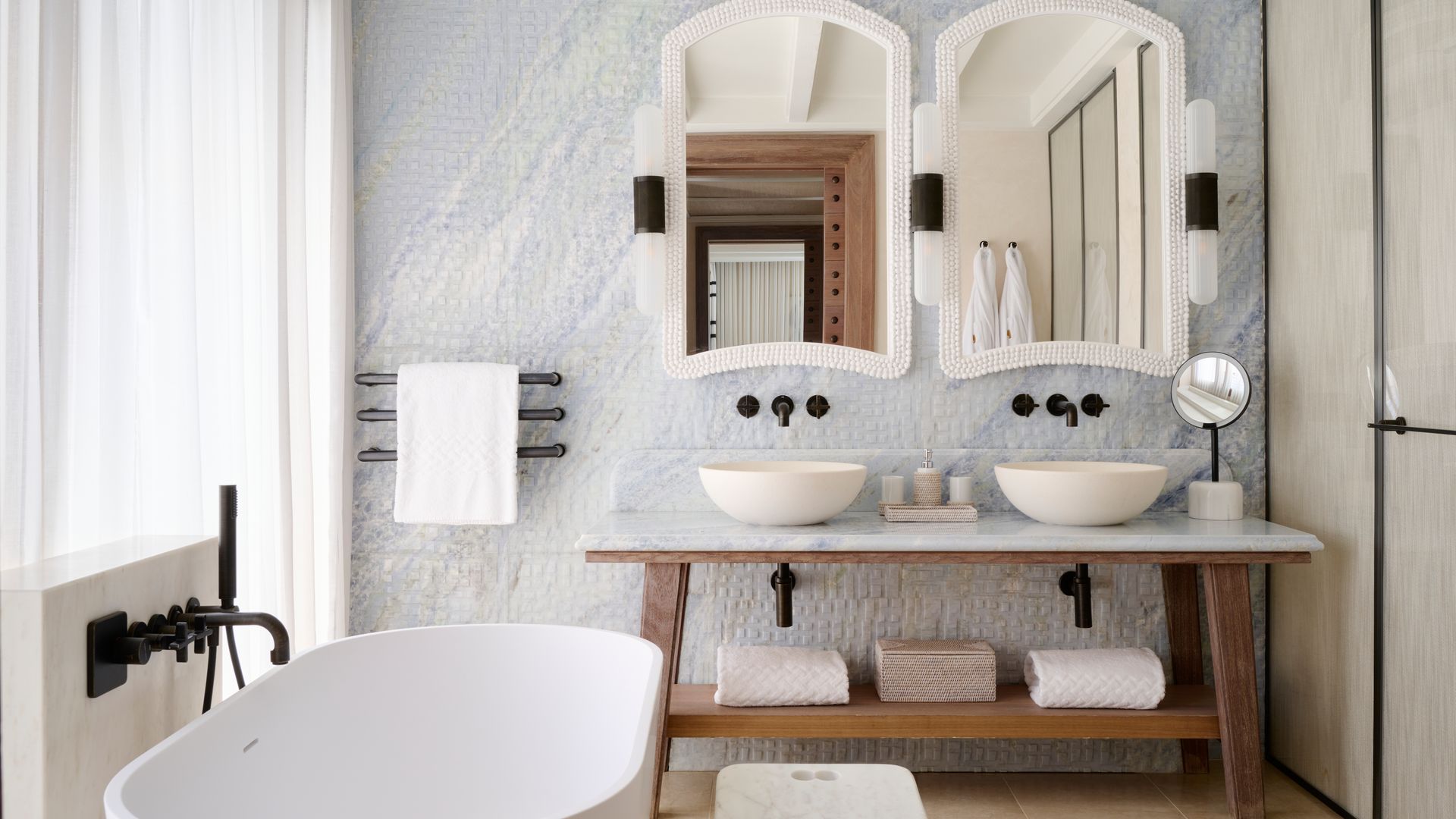 Baño con revestimiento cerámico con brillo, dos espejos con el marco blanco, bañera exenta, lavamanos sobre la encimera, grifería negra, cortinas blancas 