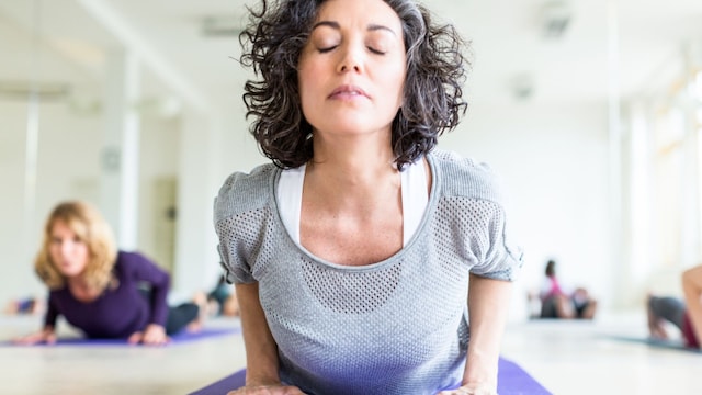 Mujer de mediana edad practicando la postura de la cobra durante su clase de yoga en el gimnasio.