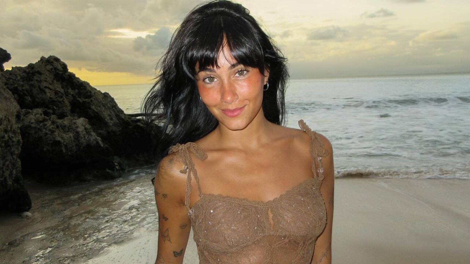 Aitana con vestido semitransparente en la playa con tatuajes en el brazo