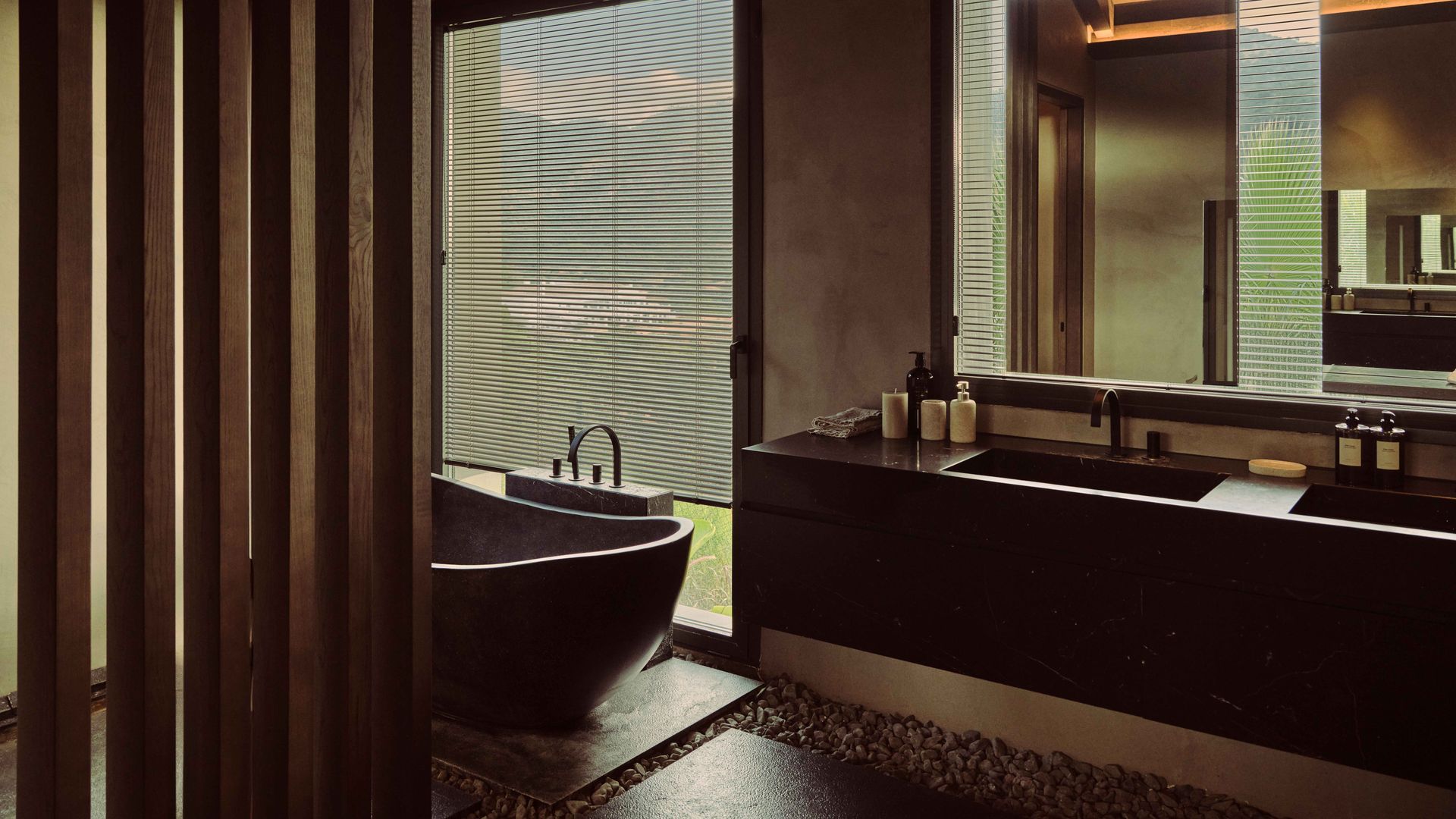 Baño con bañera exenta de estilo japonés, techo de madera, tabique de lamas de madera, espejo, luces en el techo, ventanal con cortina de lamas