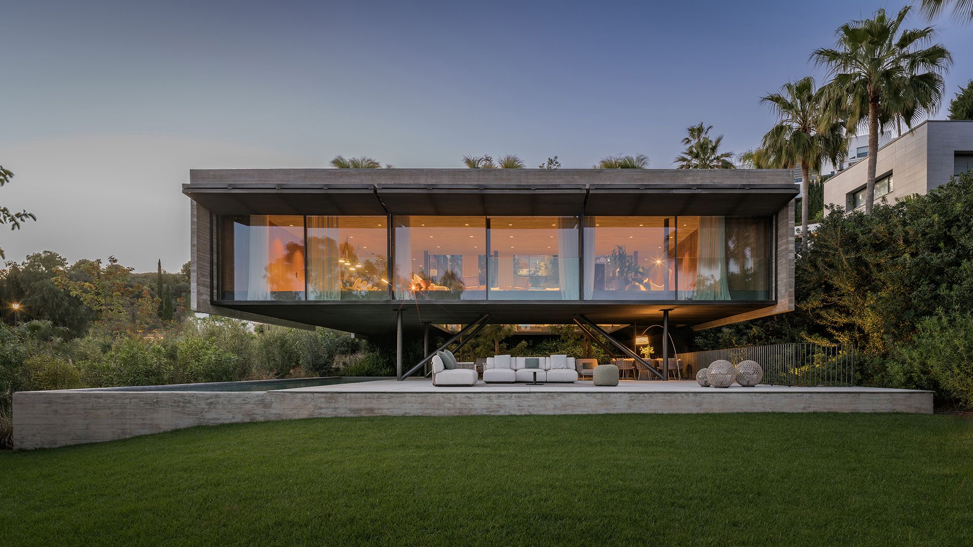 Fachada de casa moderna con tabiques de cristal, piscina y palmeras, con estar al aire libre y comedor 