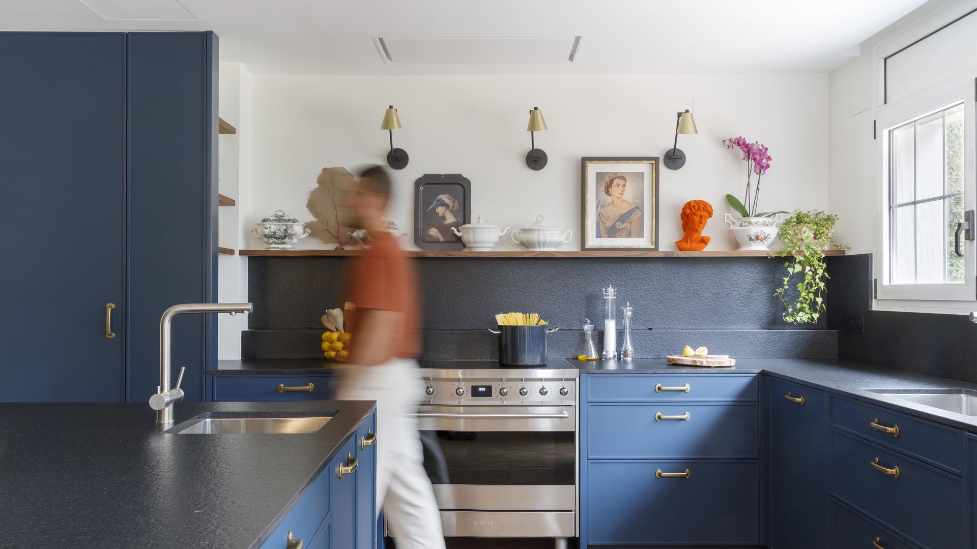 Cocina de color azul oscuro con antepecho azul, sin muebles superiores, con balda con cuadros, jarrones y objetos decorativos