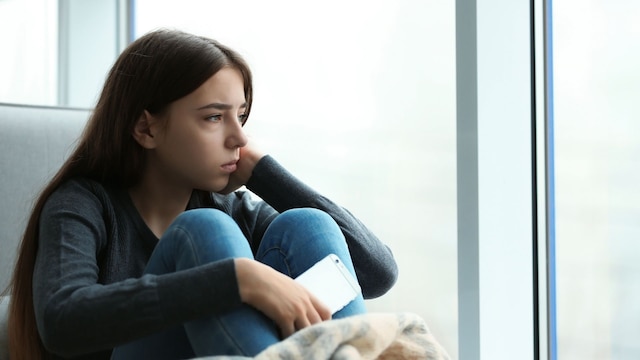Chica adolescente mirando por la ventana con cara deprimida