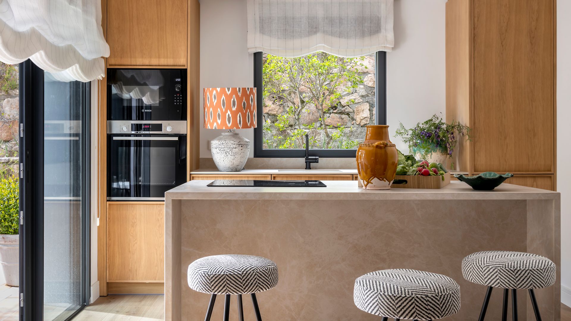 Cocina con isla y muebles de madera, salida a la terraza y estores blancos 