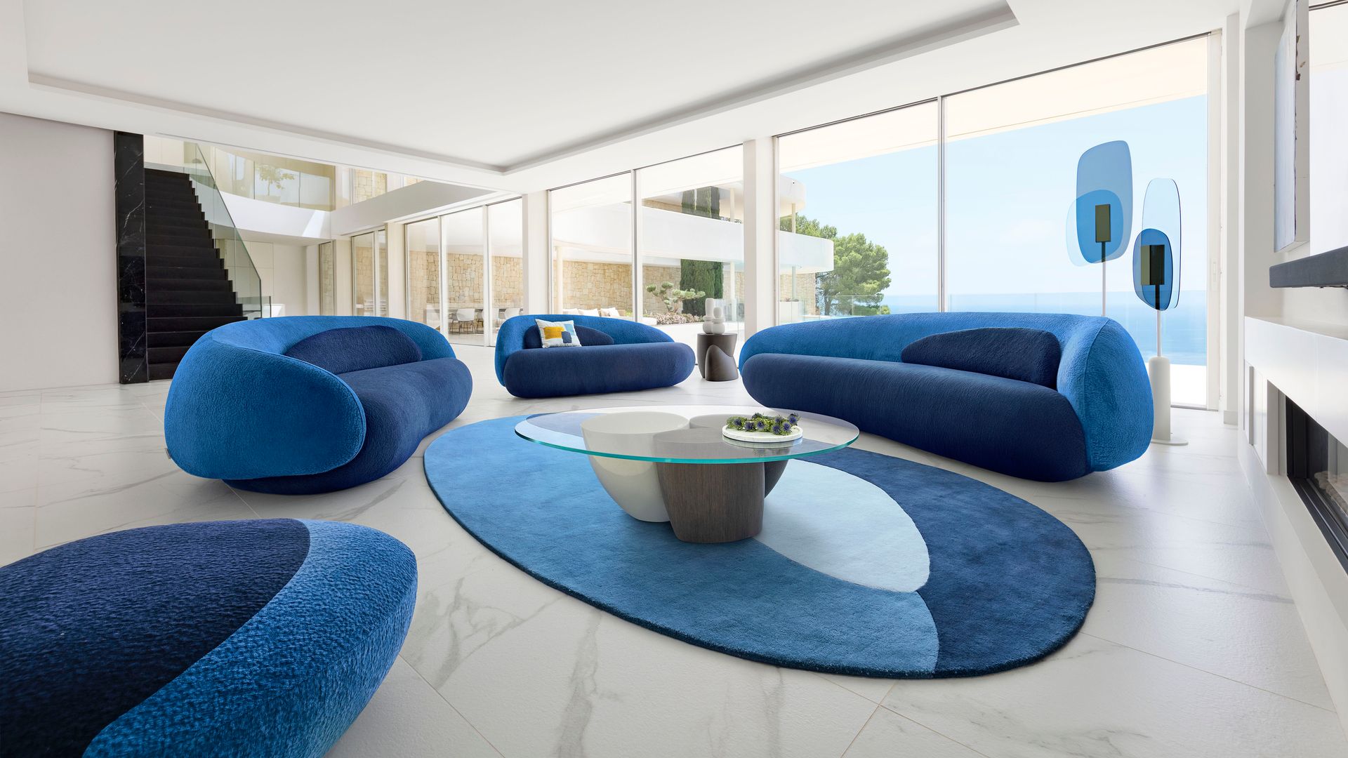 Salón XL con grandes correderas con vistas del mar con sofás azules, alfombra azul y mesa de centro de cristal 