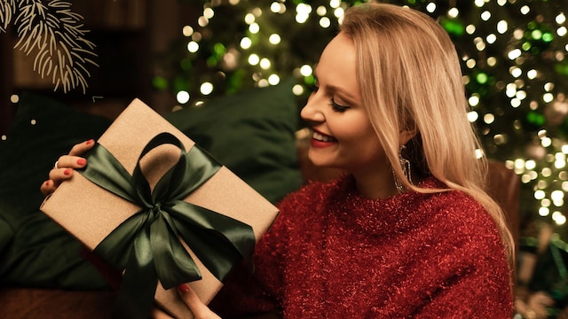 Mujer con jersey rojo y regalo junto al árbol de Navidad