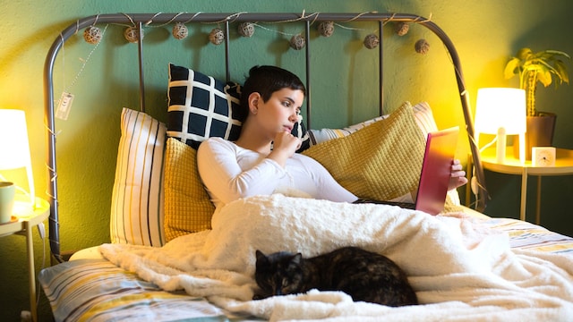 Mujer joven leyendo con gato en la cama