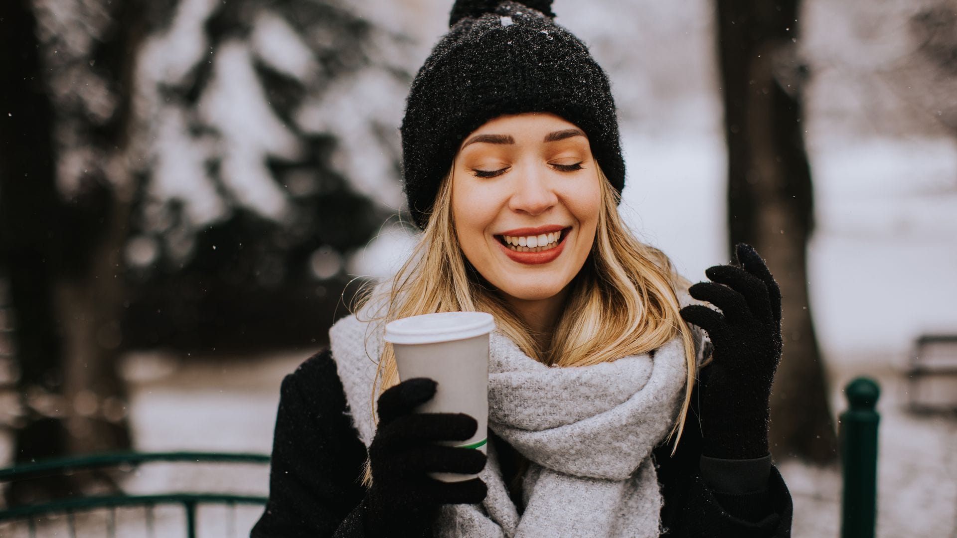 Mujer joven con gorro y guantes negros en un parque en invierno tomando café
