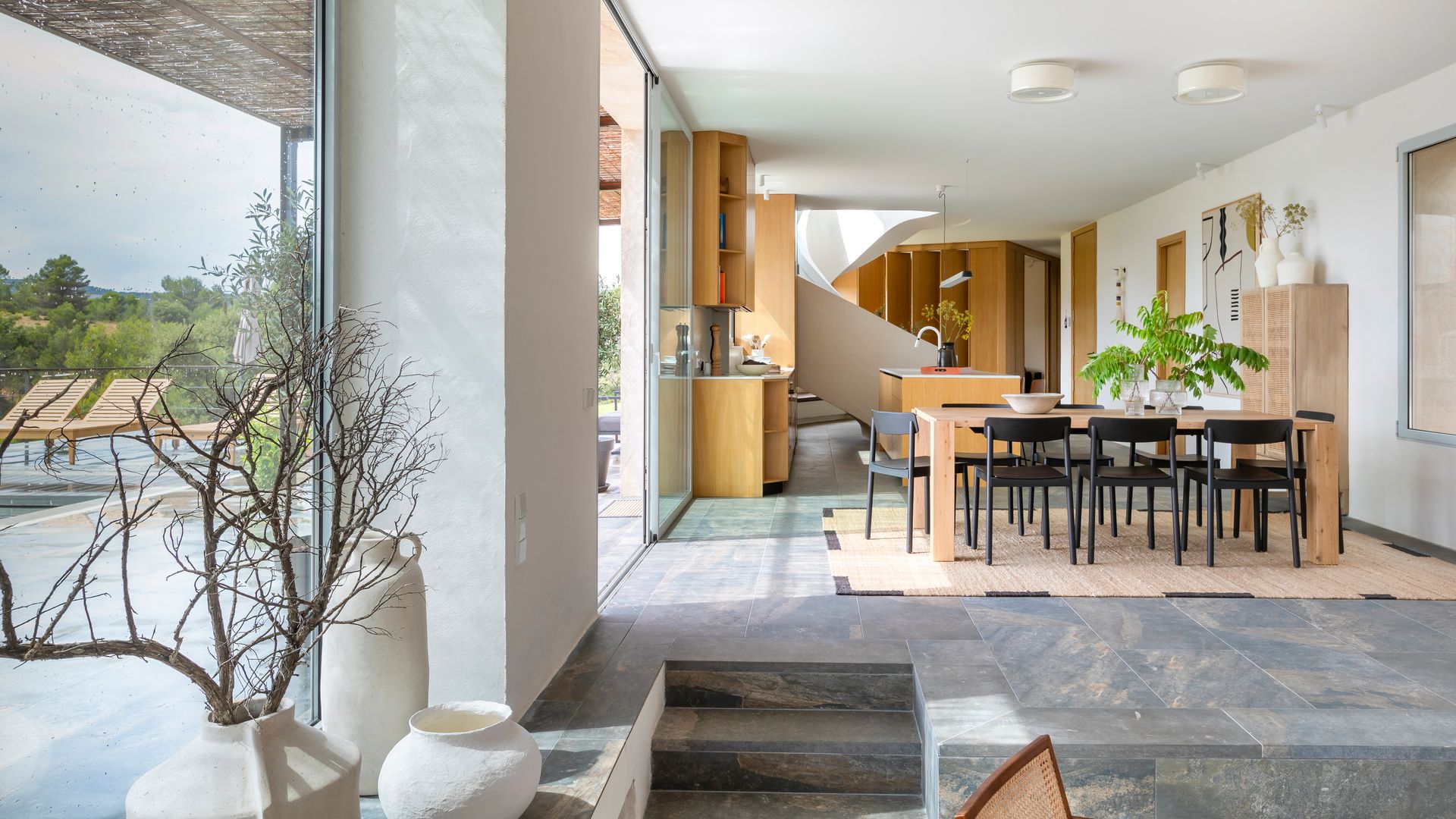 Comedor en dos alturas con suelo de microcemento, grandes ventanales, mesa de madera, sillas negras