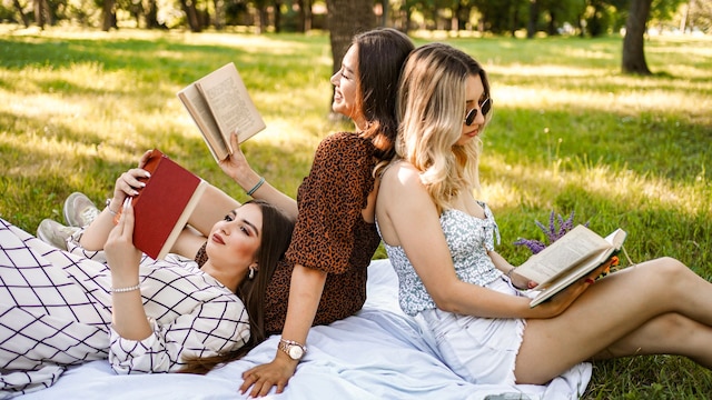 Tres amigas leyendo un libro sobre una manta en medio del campo con vestidos de primavera-verano