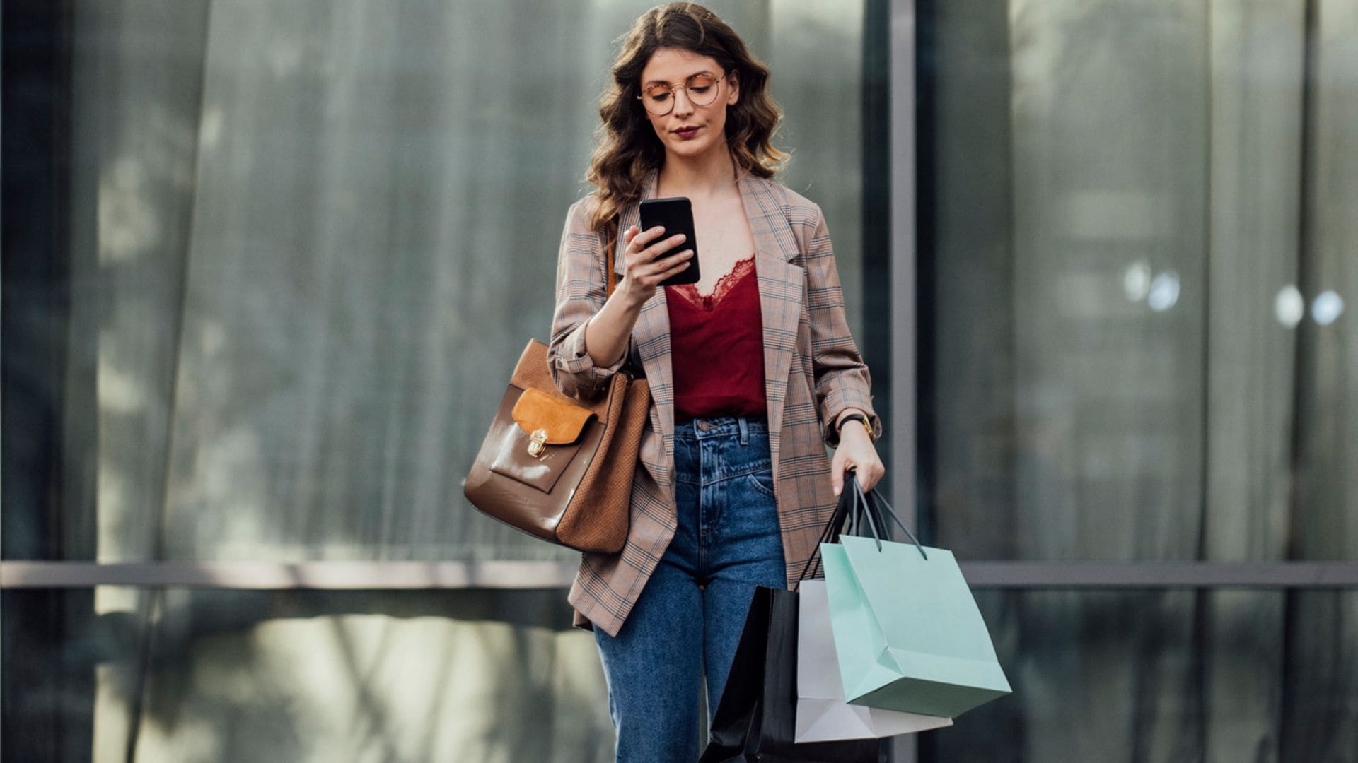 Mujer joven en la calle mirando su teléfono móvil con bolsas de compras