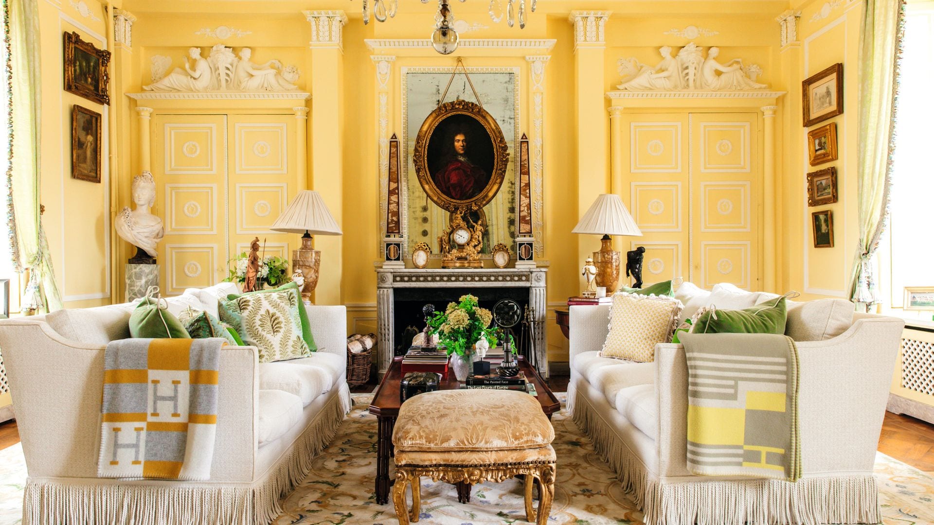 Sala de estar lujosa con sofás blancos, cojines verdes y amarillos, chimenea, y candelabro