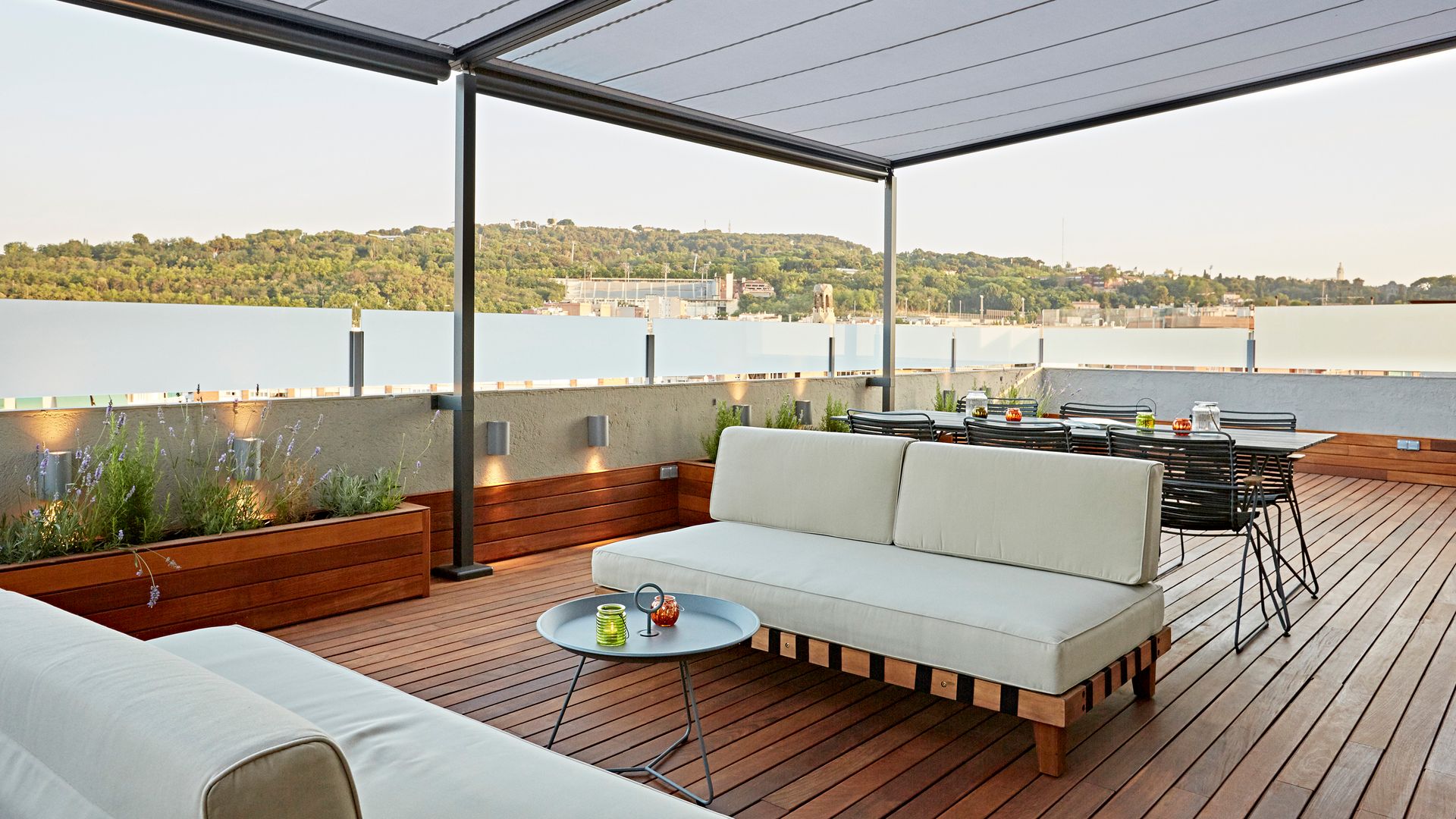 Terraza de un ático con suelo de madera, pérgola, jardineras de madera, iluminación, salón de verano y comedor 