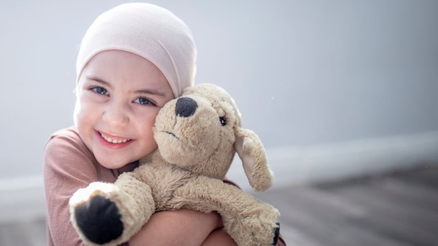 Niña con cáncer abraza, sonriente, a su peluche