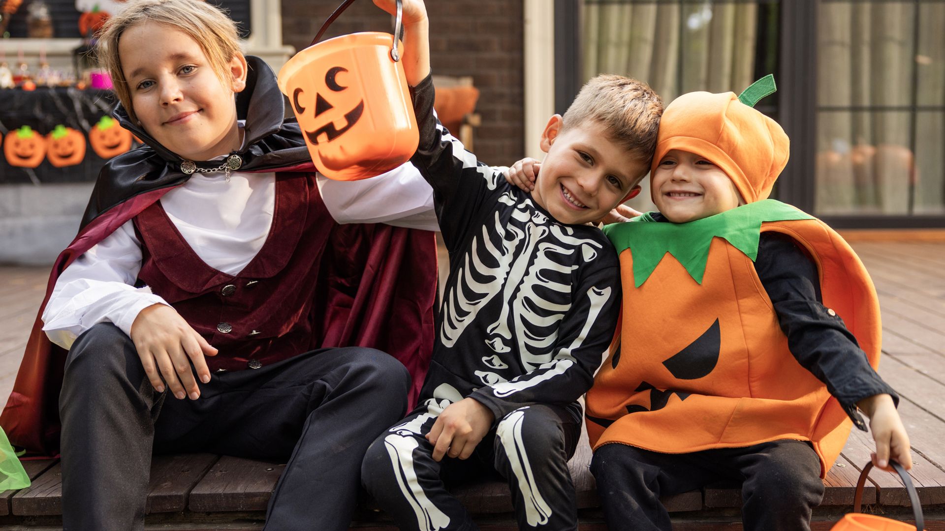 Niños sentados en el porche de su casa disfrazados de Halloween con cestas de calabaza en una fiesta.