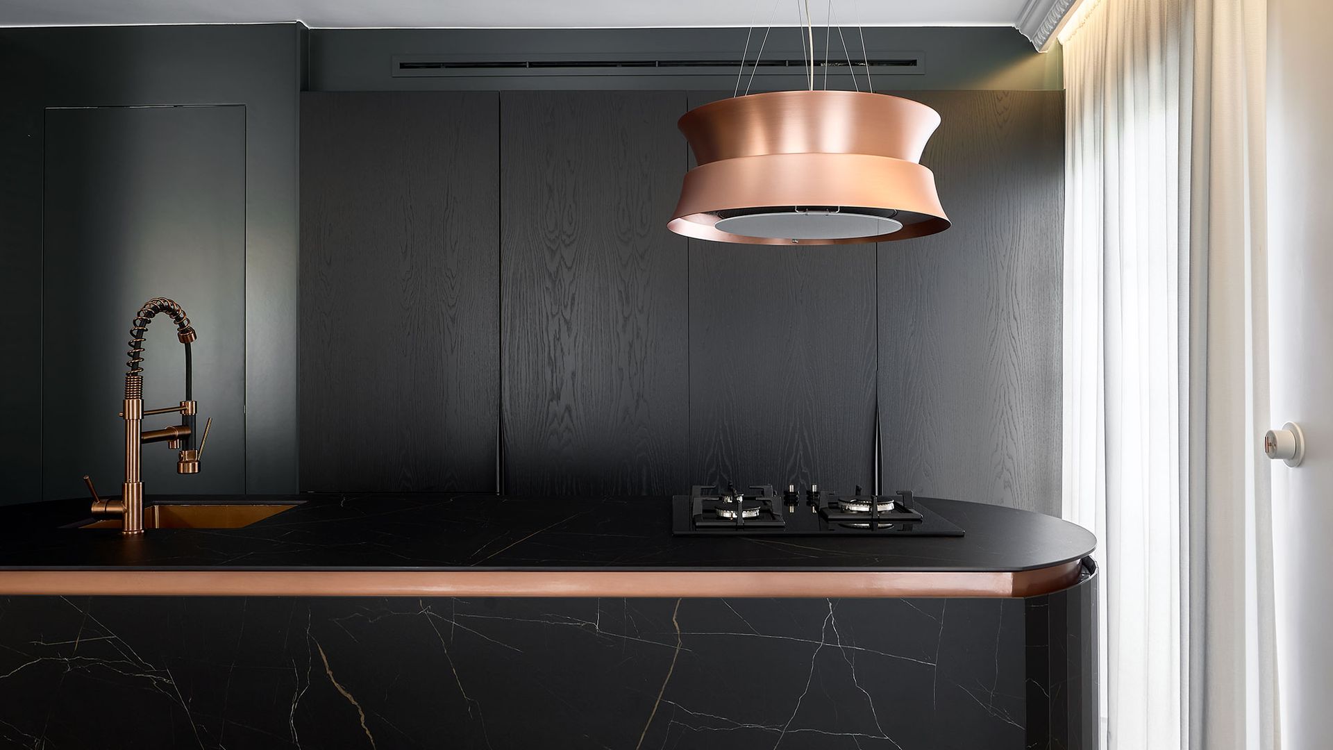 Cocina con isla negra, muebles de madera oscura, lámpara de techo rosa, grifo rosa