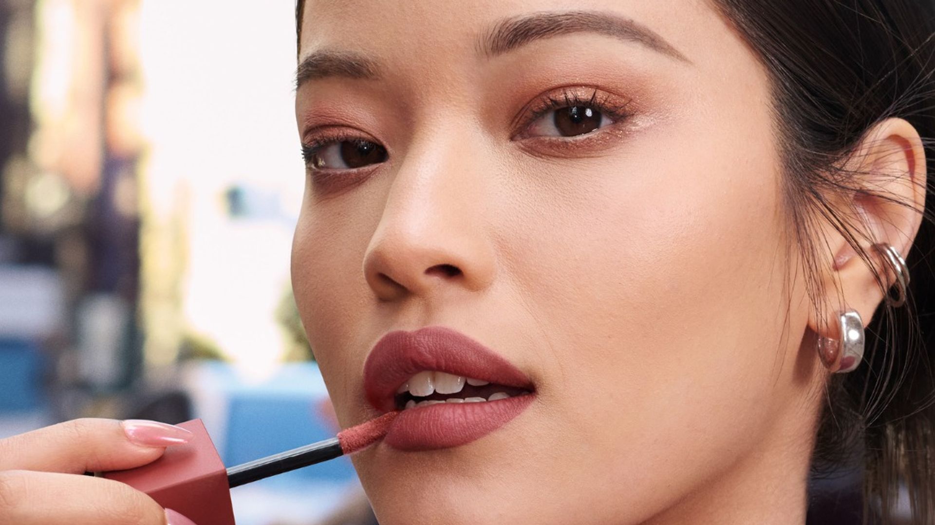Rostro de mujer asiática en la calle aplicándose labial de Maybelline