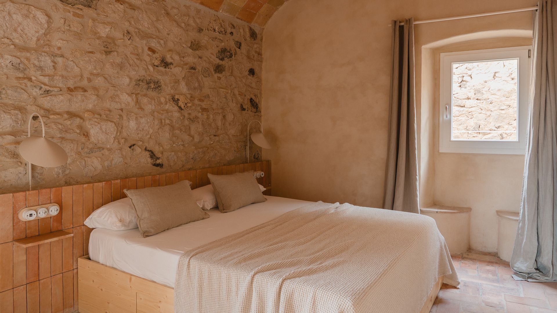 Dormitorio con techo abovedado, cabecero de gres, banco bajo la ventana, cortina, cama de madera