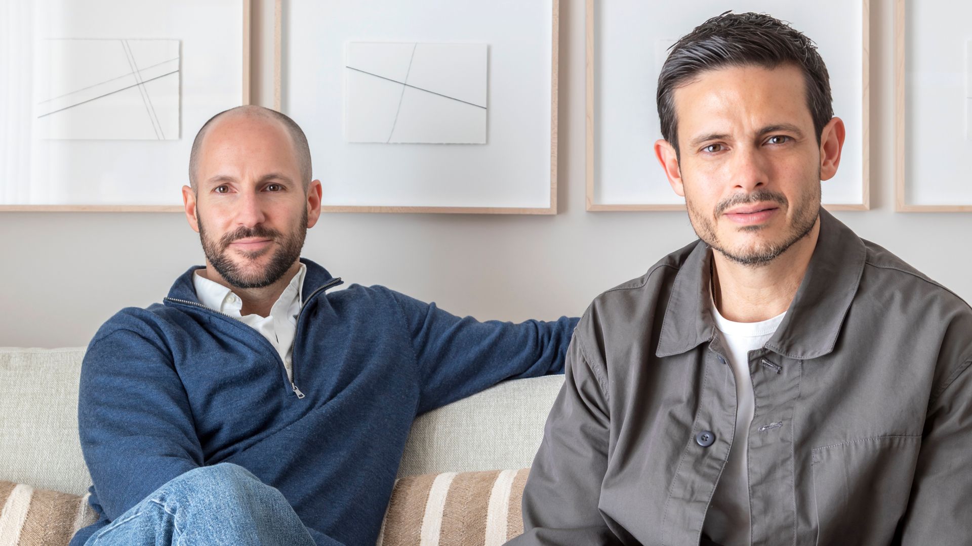Retrato de interioristas del estudio Punto M, sentados en sofá, con pared de cuadros