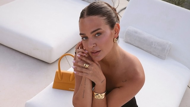 Laura Escanes con vestido negro estampado de Desigual, sandalias plateadas y bolso Jacquemus sentada en una tumbona