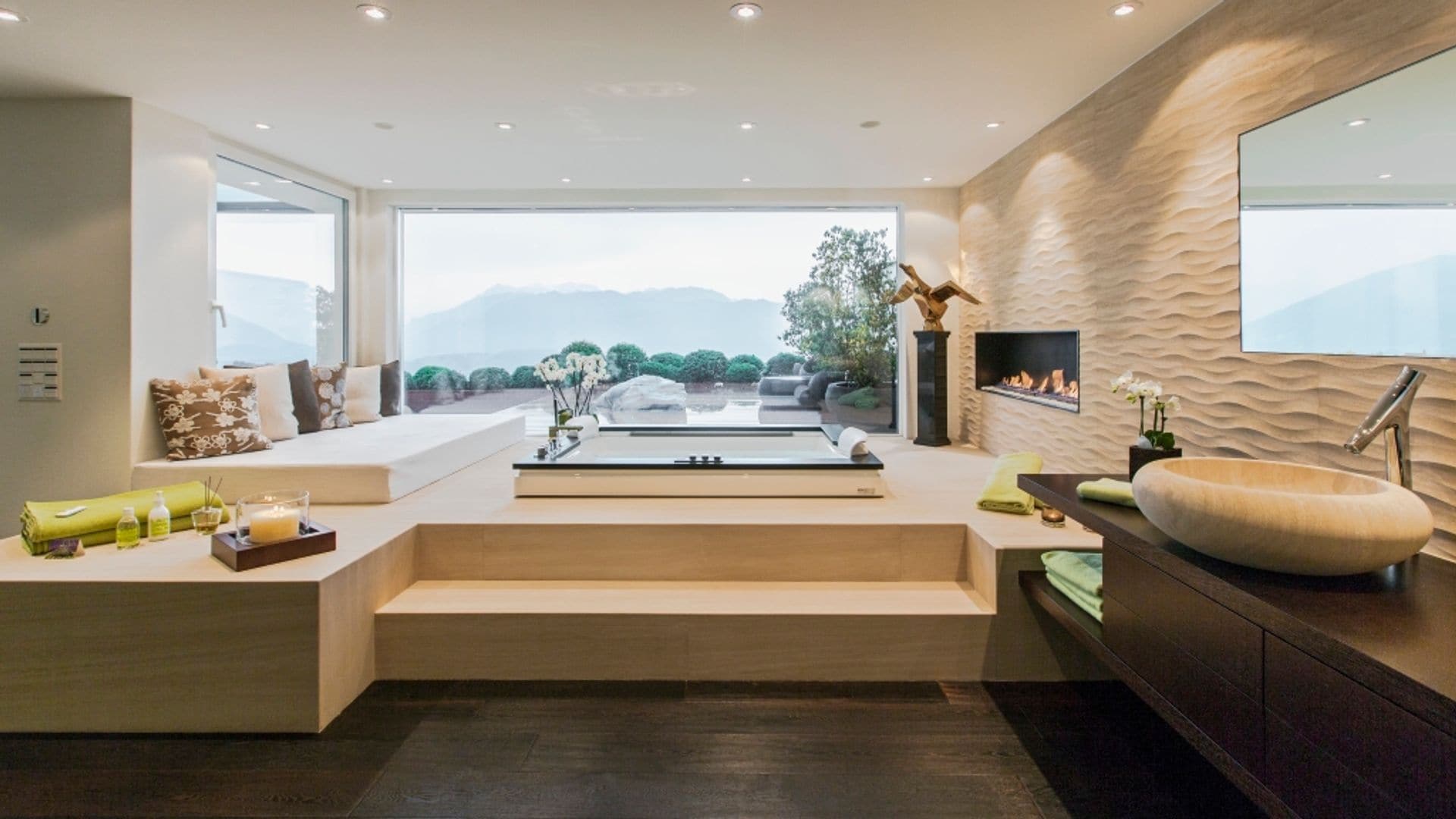 Baño de estilo japonés con bañera empotrada en el suelo, separada de la zona de tocador por dos escalones, grandes ventanales con vistas al jardín, focos empotrados techo, lavabo de piedra