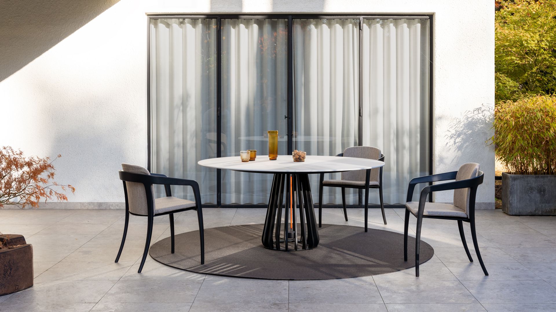 <comedor de verano con alfombra redonda, mesa y sillas negras, ventanal con perfiles negros y cortinas blancas