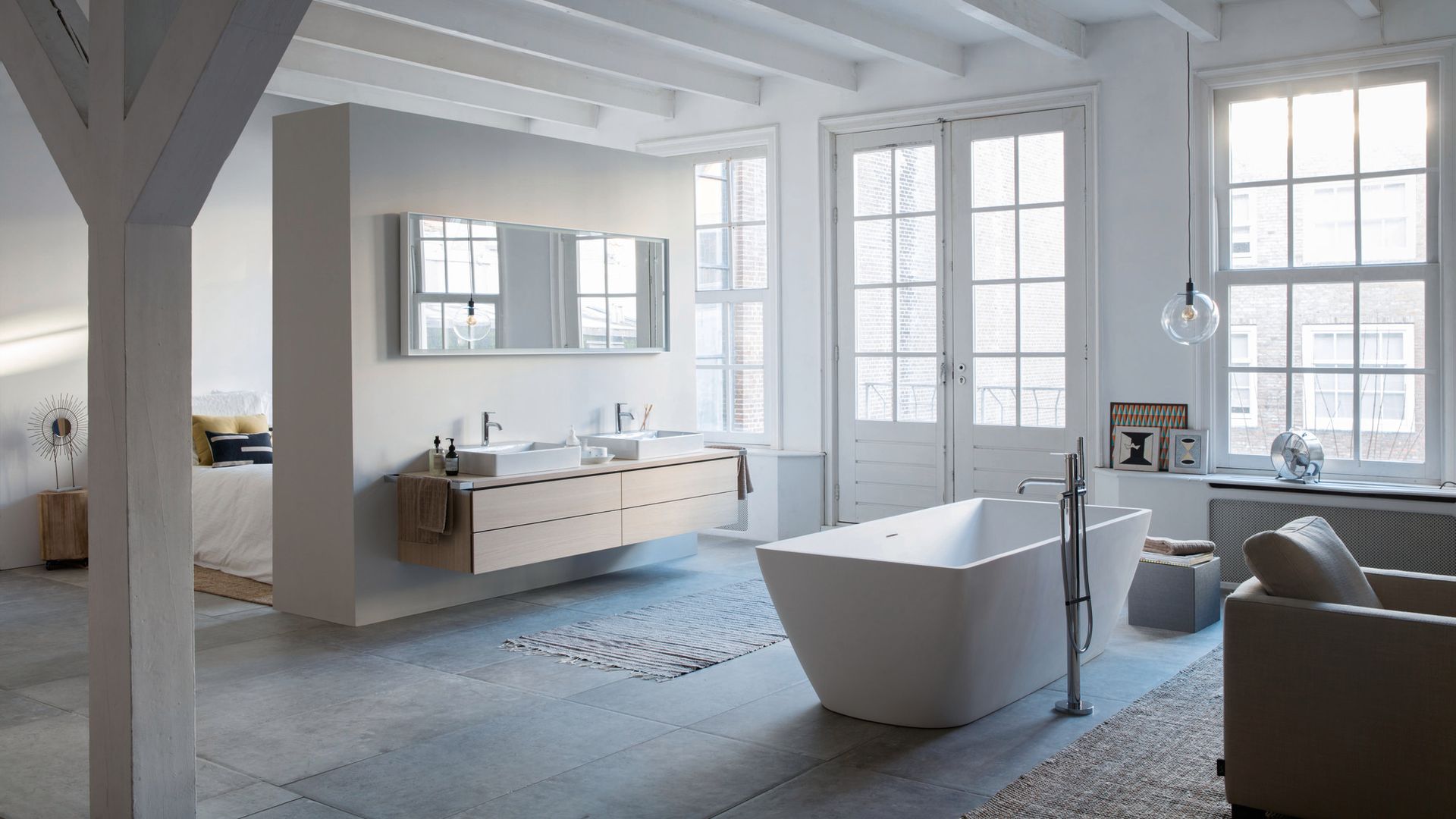 Baño muy grande abierto al dormitorio con bañera exenta, grandes ventanales. vigas de madera blanca en el techo, mueble bajolavabo suspendido, espejo 