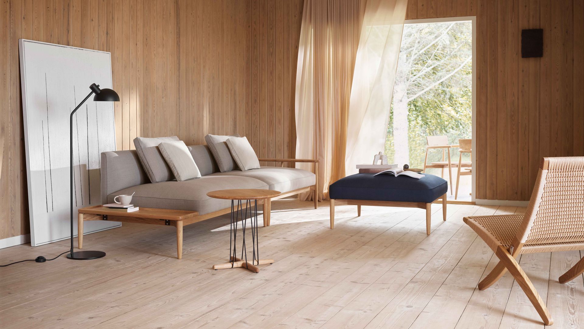 Salón con suelo y paredes de madera, cortinas, sofá gris con mesa auxiliar, mesa de centro tapizada en azul