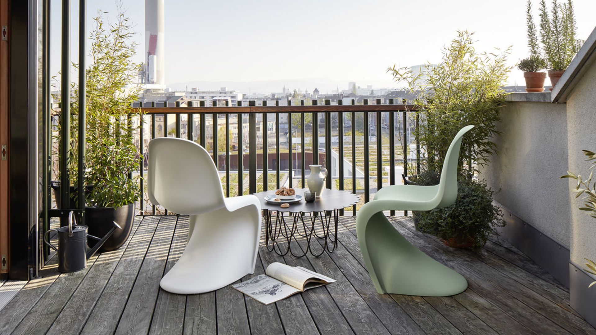 Terraza pequeña con sillas Panton blanca y verde, suelo de madera, macetas 