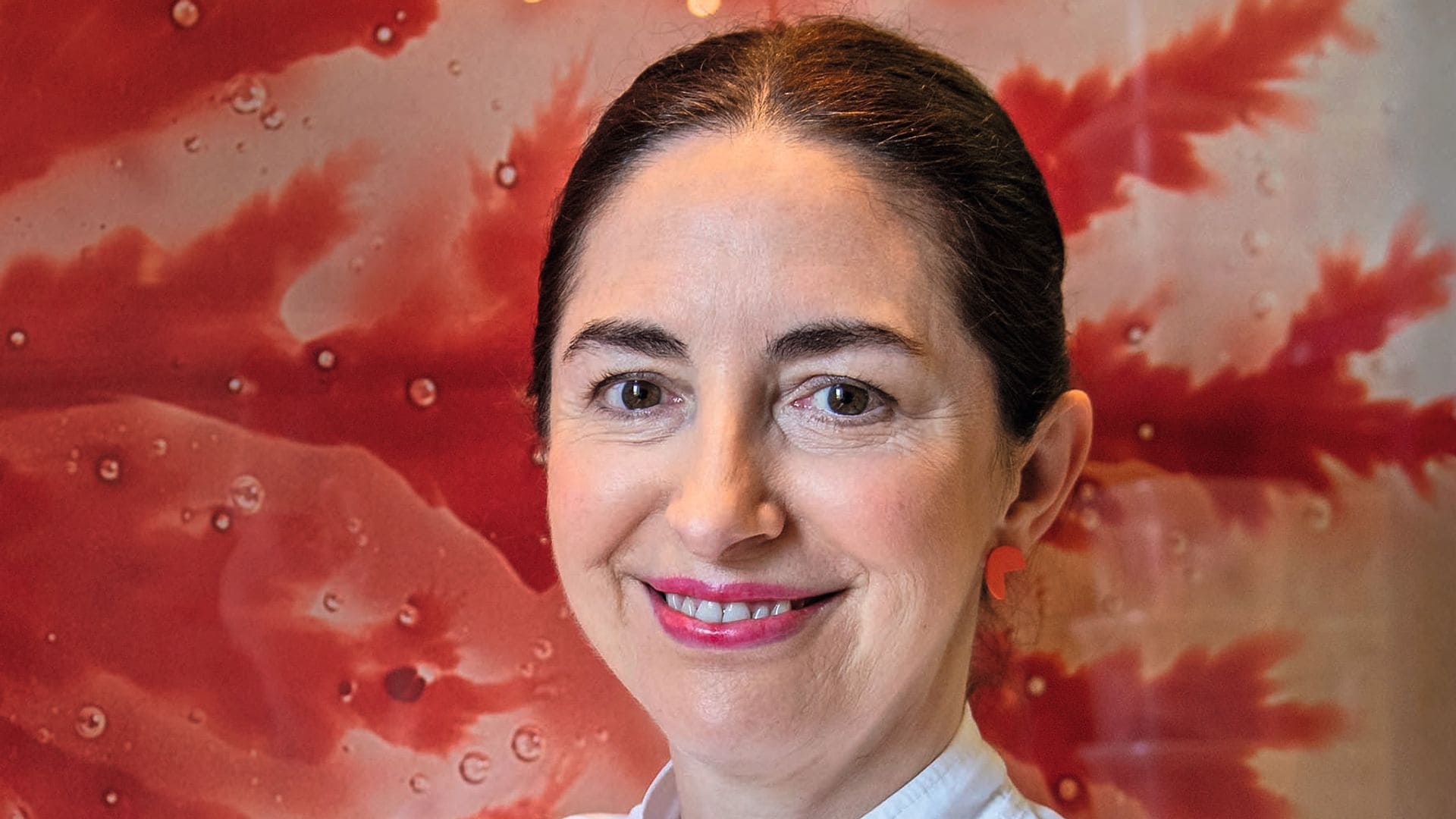 Elena Arzak, con uniforme de chef blanco, sonríe con brazos cruzados frente a un mural rojo.