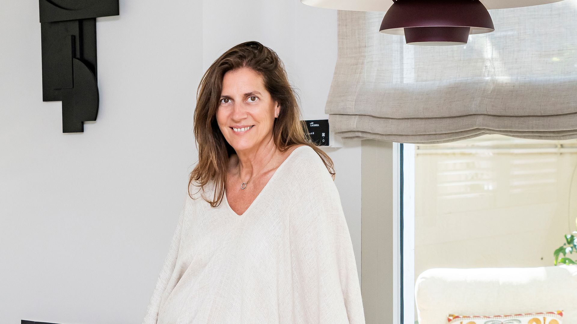 Retrato de la interiorista Elena Navarro, apoyada en una mesa de comedor de madera, delante de una chimenea 