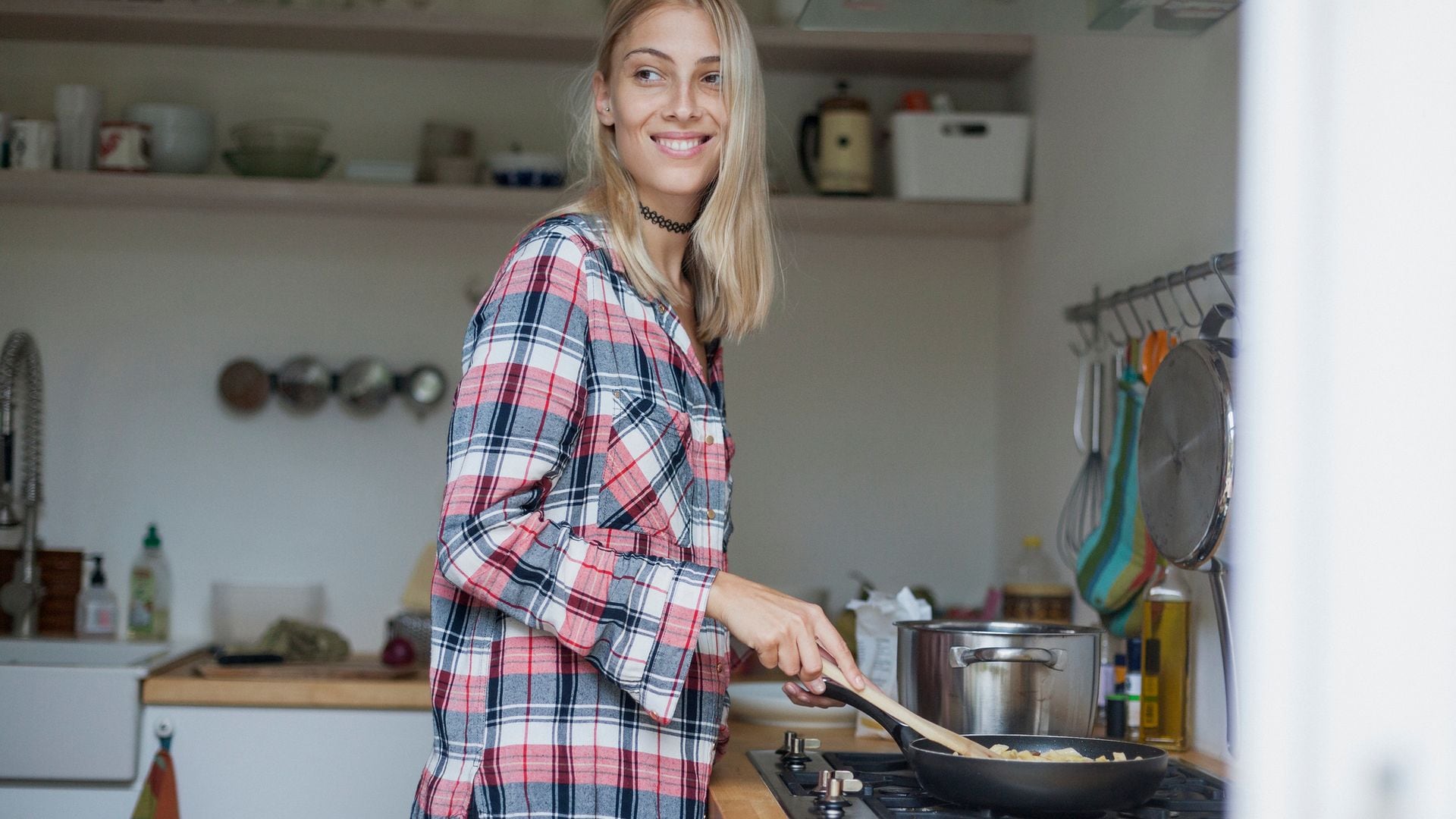 Mujer cocinando en su cocina, en la encimera con una cuchara de palo removiendo la comida de su sartén.