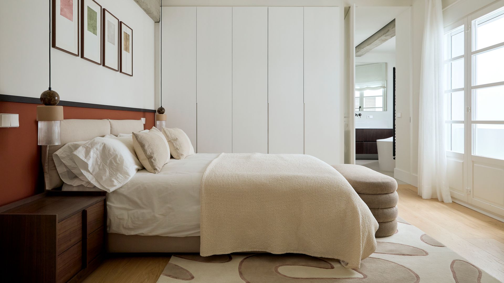 Dormitorio con armario blanco de suelo a techo, cabecero de color marrón, cortinas hasta el suelo, alfombra XL de motivos geométricos, mesita de noche de madera oscura