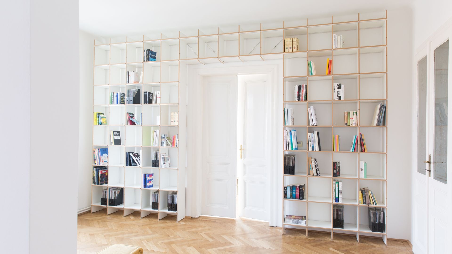 Estantería de madera blanca rodeando la puerta de paso, suelo de madera en espiga