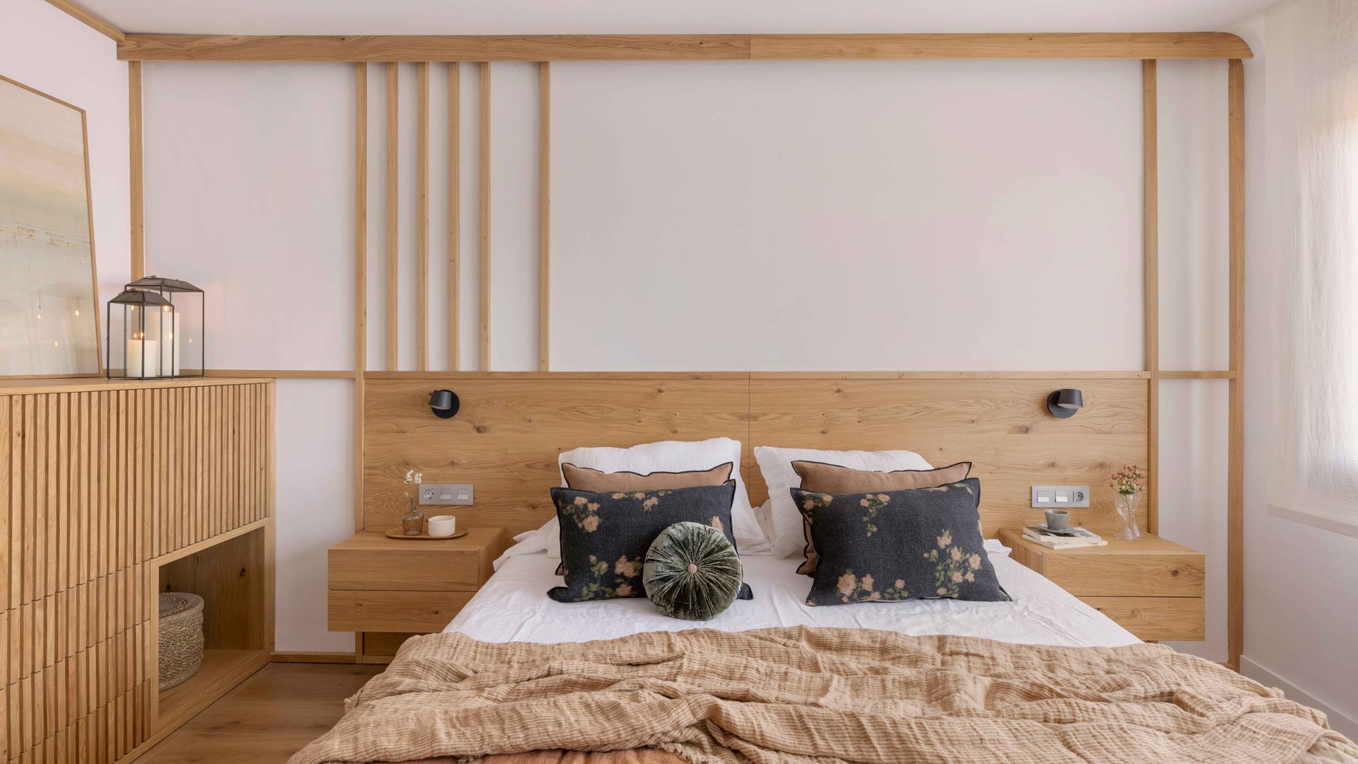 Dormitorio de estilo japandi con estructura de madera que hace las veces de cabecero e incluye estantería, ropa de cama de lino, cojines 