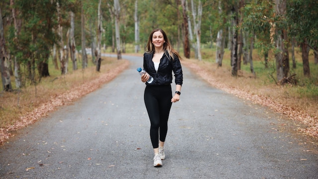 chica joven caminando por un parque con una botella de agua