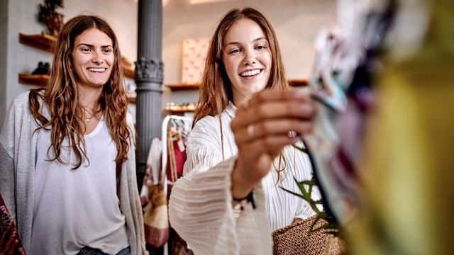 Dos mujeres haciendo compras en una tienda sonriendo, mientras miran prendas.